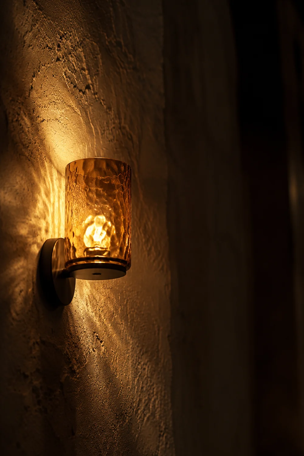 Amber glass wall sconce mounted low on textured plaster wall casting warm light and shadow