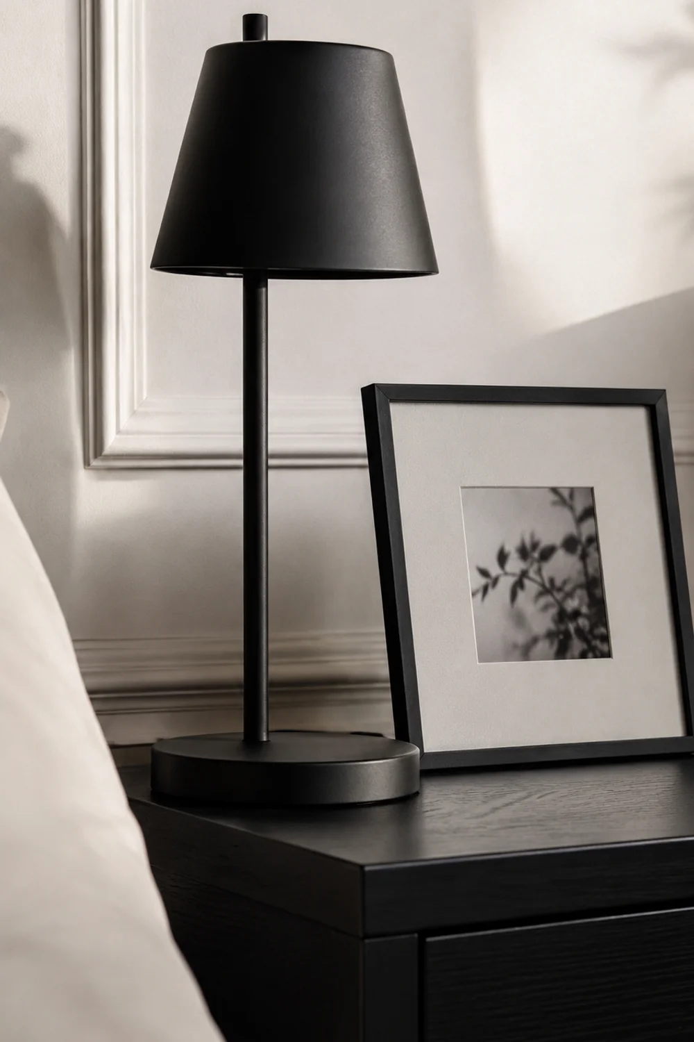 Matte black lamp and picture frame accent on a white Scandinavian nightstand