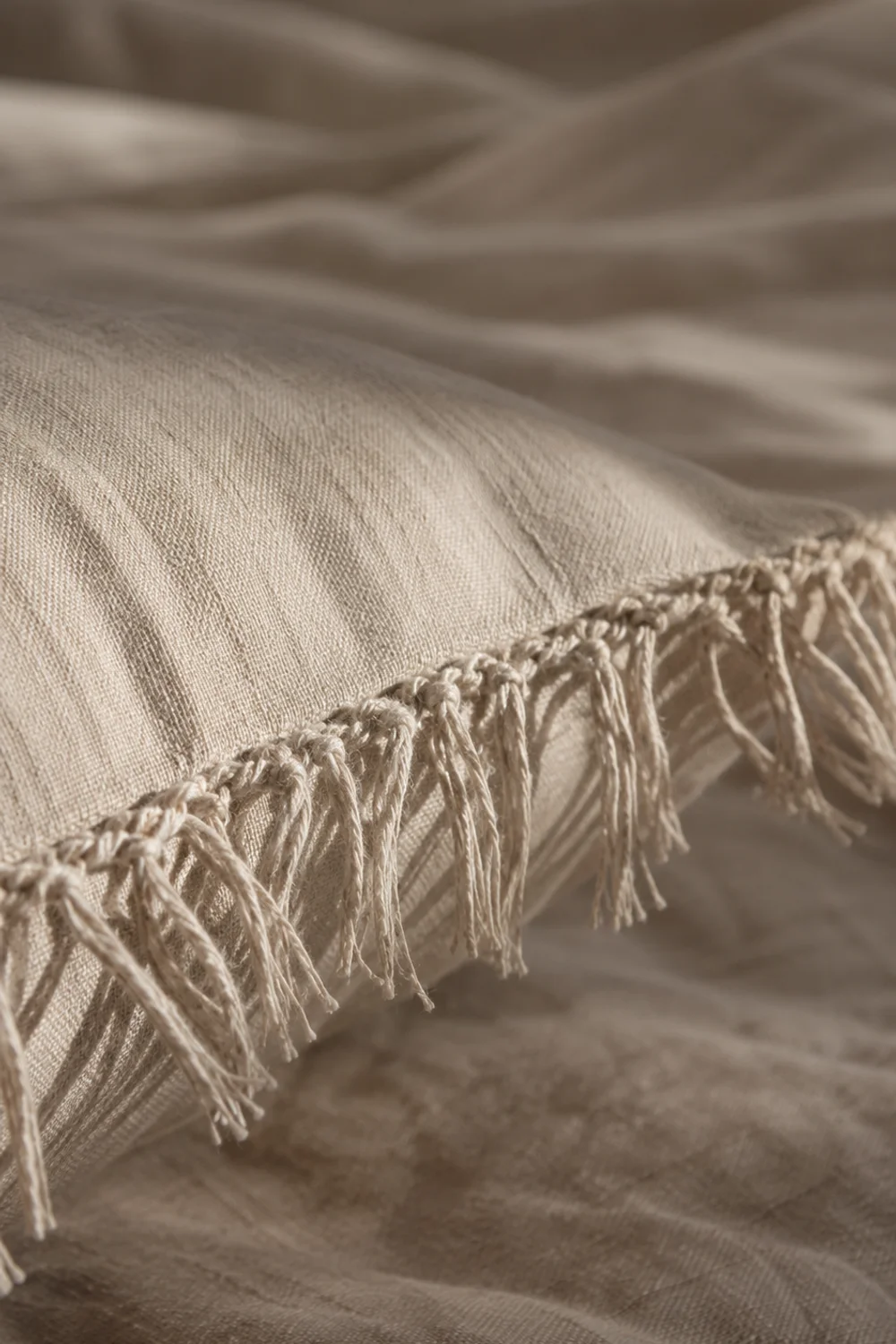 Macro detail of hand-knotted cream fringe trim along the seam of a linen throw pillow