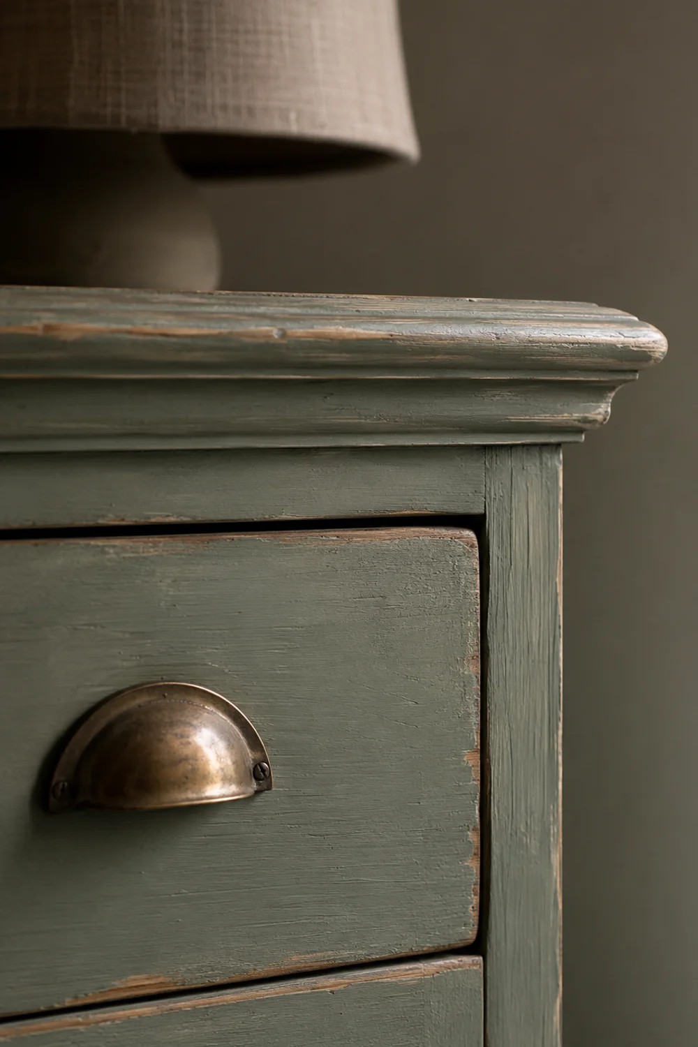 Close-up of chalky sage-green milk paint finish on a dresser corner with worn edges