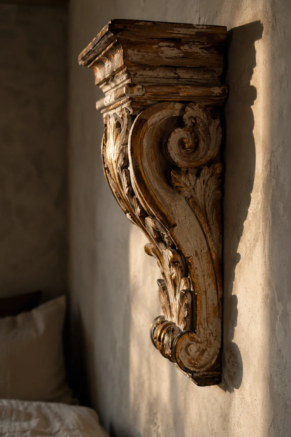 Reclaimed carved wood architectural corbel mounted above a bed casting deep shadow