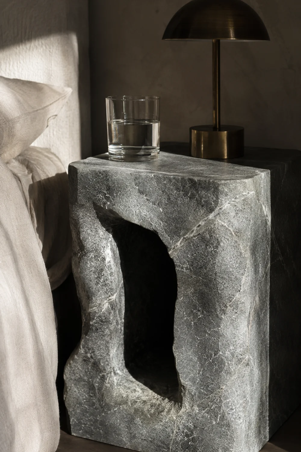 Hand-carved solid soapstone side table beside a low bed with reading lamp