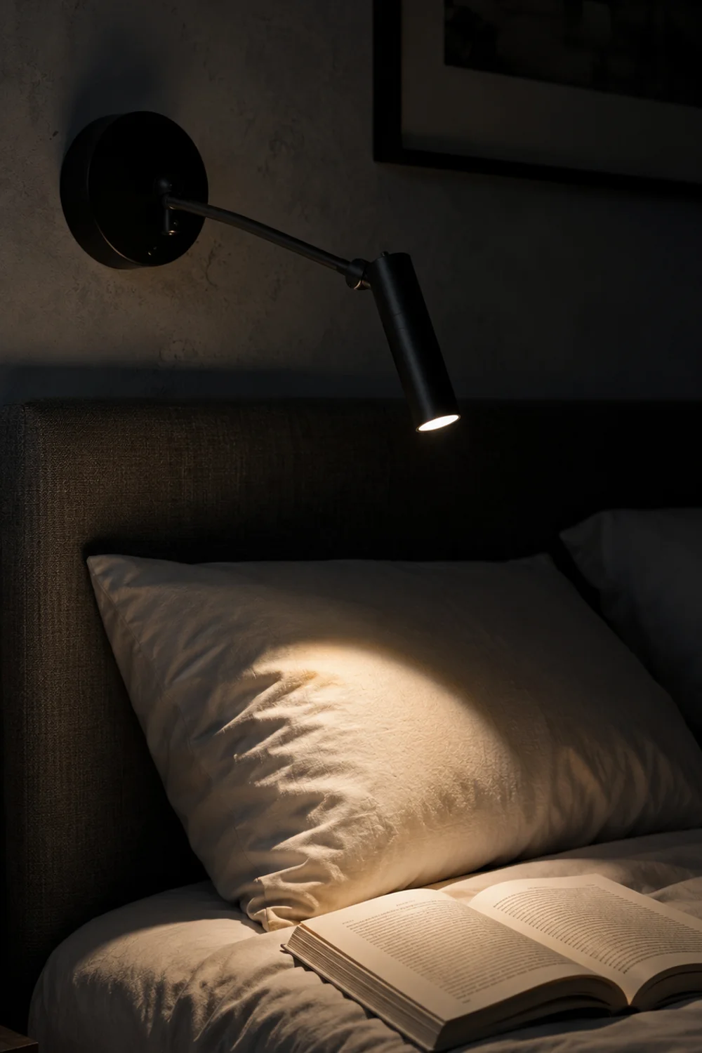 Adjustable swing-arm wall reading light focused narrowly on an open book above the bed