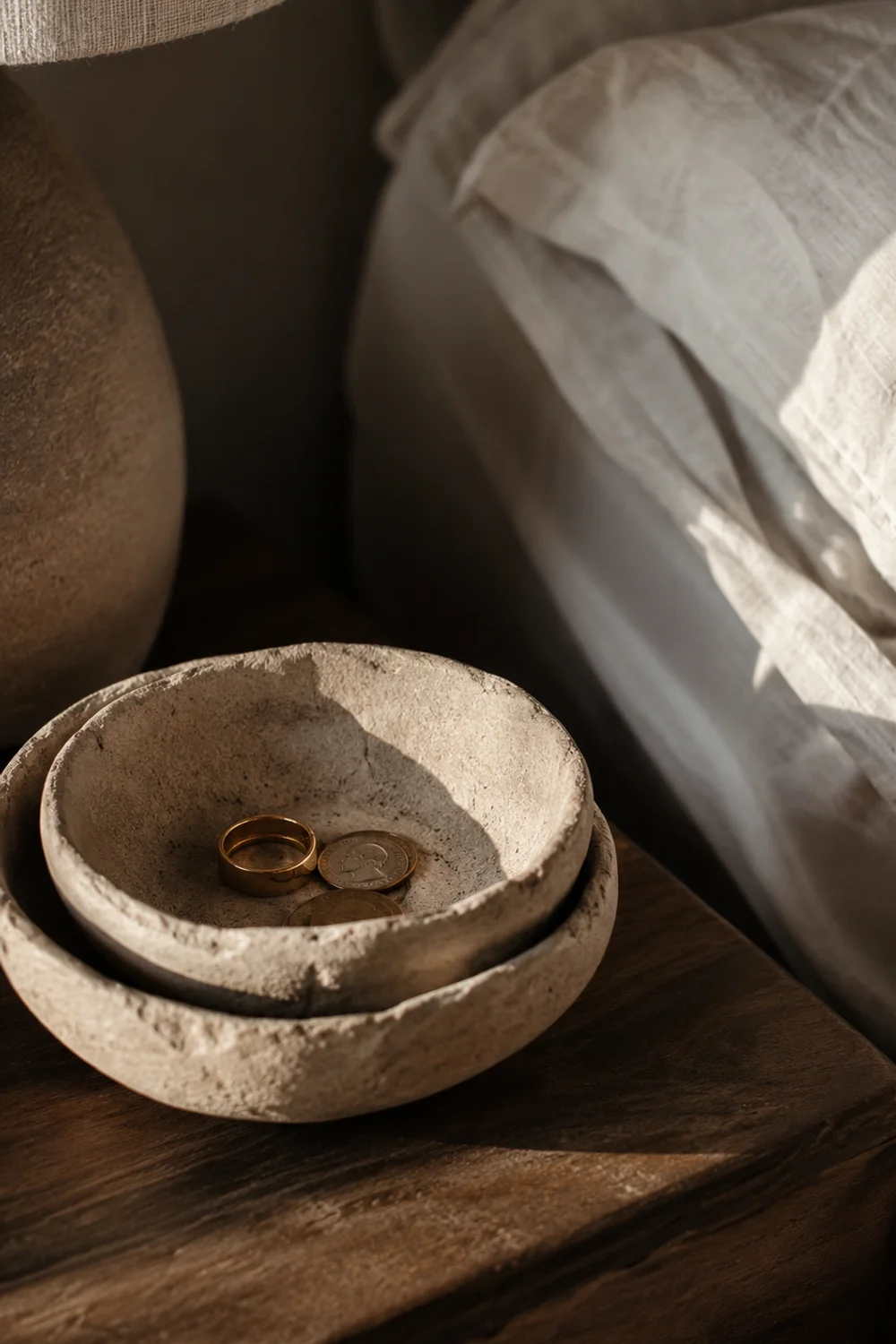 Unglazed stoneware catchall bowls with raw clay texture on a bedroom nightstand