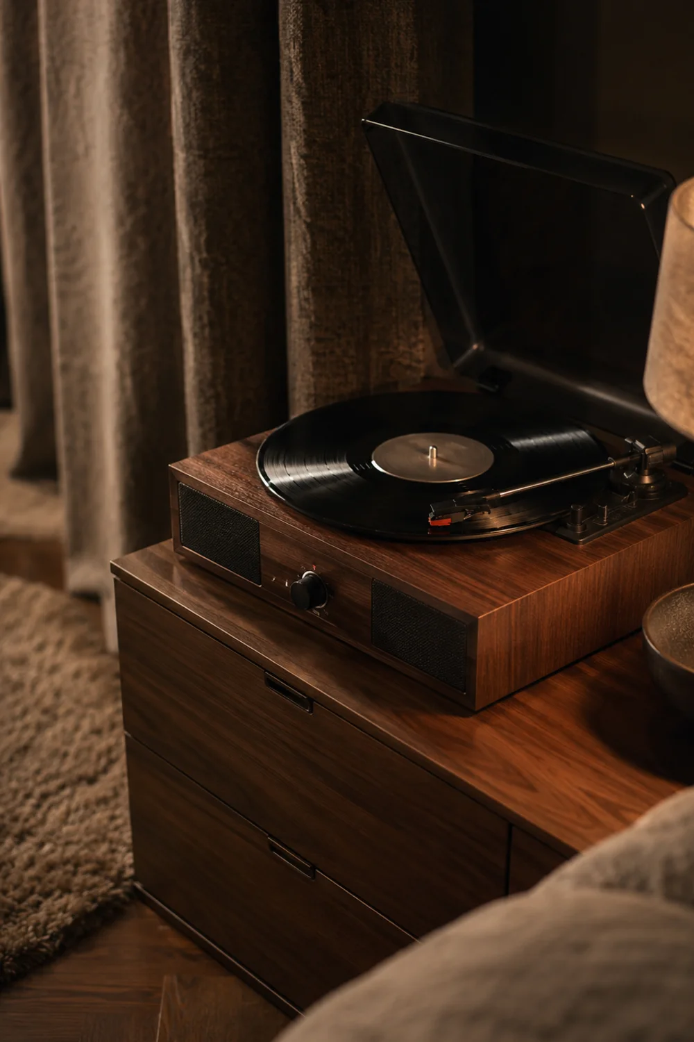 Compact walnut record player with built-in speakers playing on a low bedroom dresser