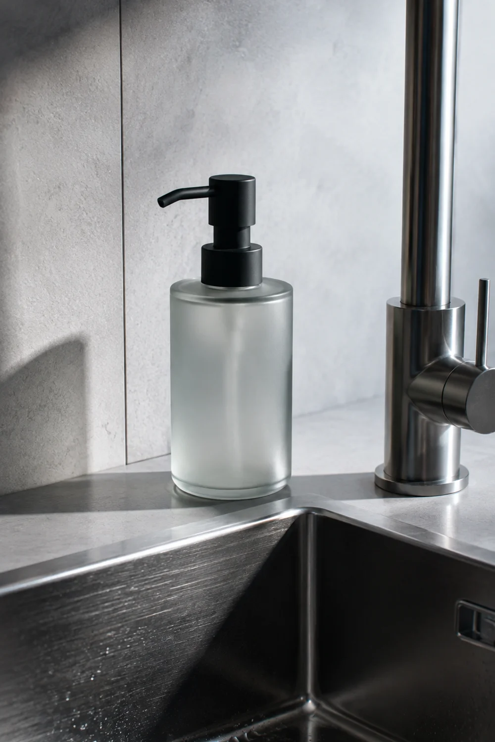 Single frosted glass soap dispenser beside a clean kitchen sink