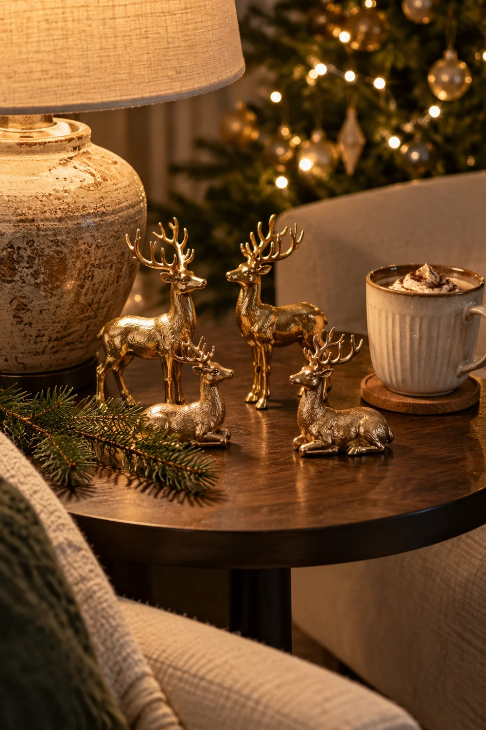 Four small gold resin reindeer figurines, two standing and two sitting, grouped on a side table beside a lamp and mug